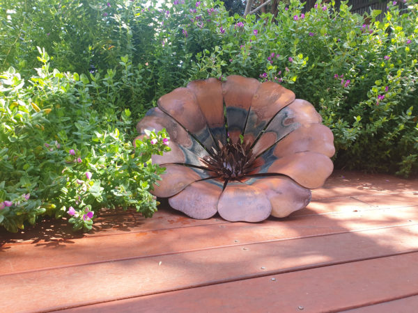 Handcrafted Sun Flower rusted metal art in a garden, featuring a rich orange and red patina, 50 cm diameter.