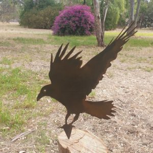 A beautiful Crow Garden Stake crafted from durable Corten steel, standing 340mm tall, showcasing rust hues in an outdoor garden setting.