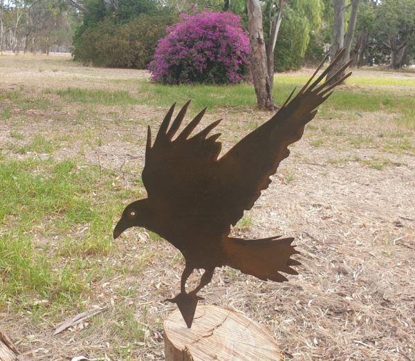 A beautiful Crow Garden Stake crafted from durable Corten steel, standing 340mm tall, showcasing rust hues in an outdoor garden setting.