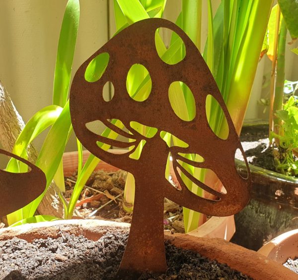 A rusted metal garden sculpture of a tall mushroom. Laser-cut from Corten steel, it stands 30 cm high and 18 cm wide, featuring a natural weathered patina. Perfect for garden beds or potted plants.