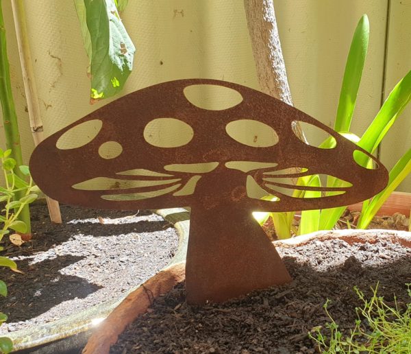 A rusted metal Mushroom Wide garden sculpture made from 1.6mm Corten steel, measuring 30cm x 27cm, including its attached spike. It adds a rustic, fairy-tale charm to garden beds or pots, with a natural orange-red patina.