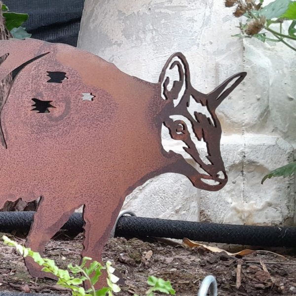 Numbat Garden Stake in Garden: The Numbat Garden Stake stands proudly in a flower bed, showcasing its laser-cut design and vibrant rust finish amidst blooming plants.