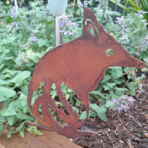 Bandicoot Garden Stake in Corten steel, showcasing its rusted orange-red color in a garden setting.